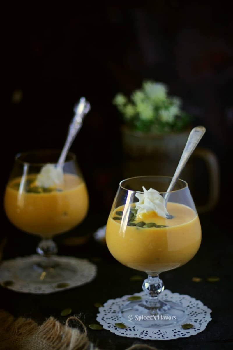 pumpkin custard served in glasses with whipped cream pumpkin seeds and a spoon in the picture