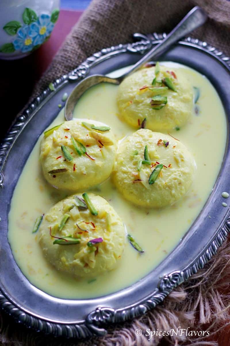 rasmalai pieces placed on an antique oval shaped plate on a wooden cutting board