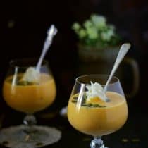 pumpkin custard served in glasses with whipped cream pumpkin seeds and a spoon in the picture