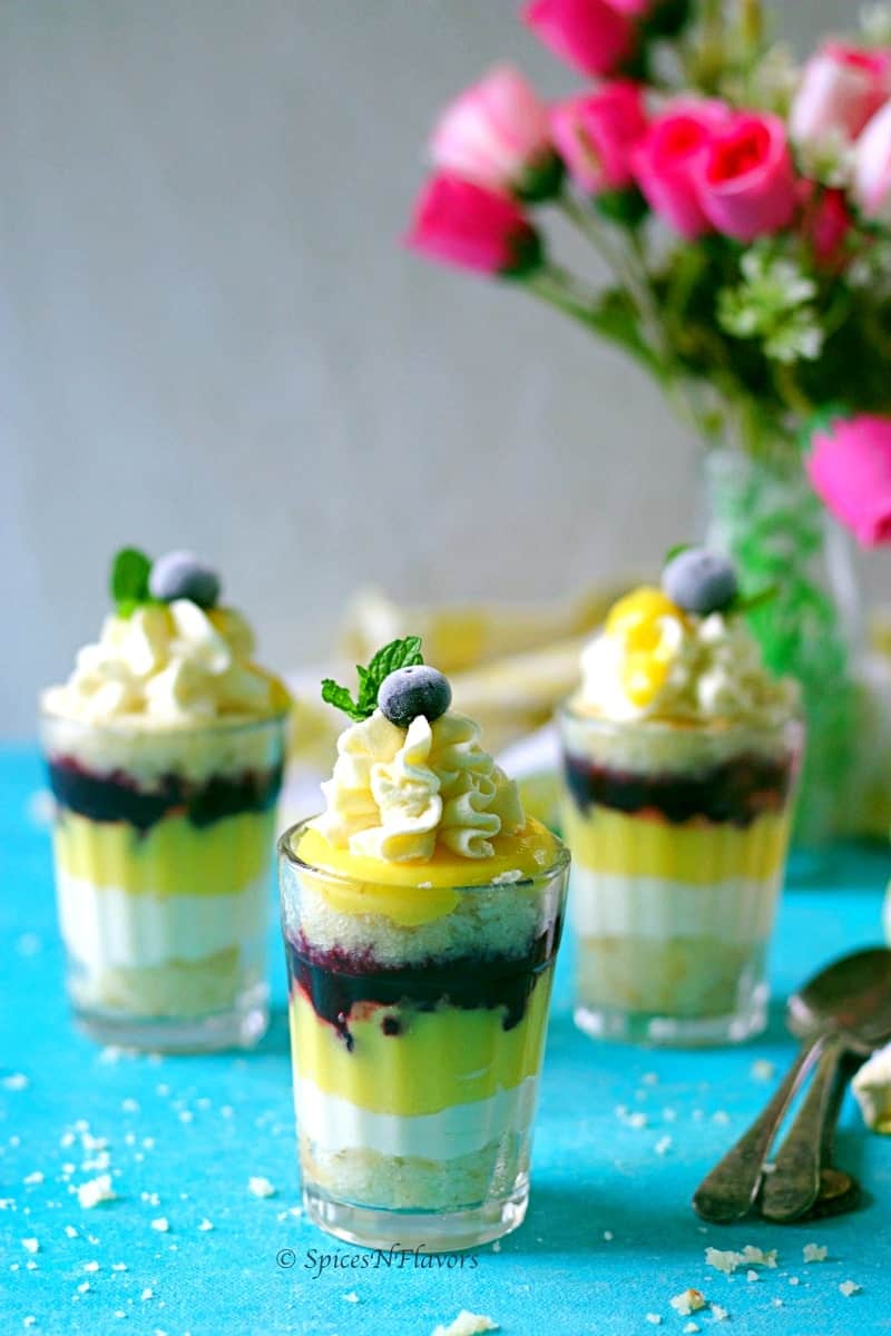 layers of cake, whipped cream, lemon curd and blueberry compote arranged in a tea glass