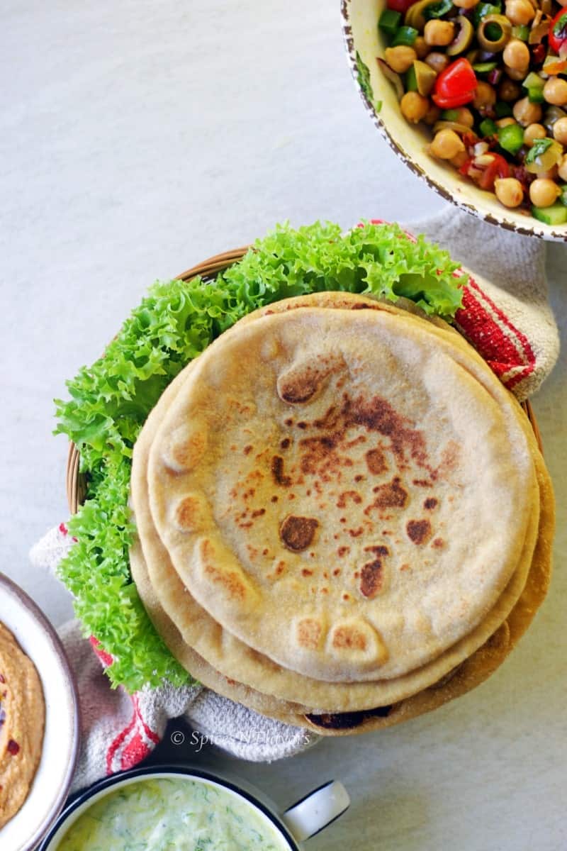 overhead view of whole wheat pita bread placed in a brown basket with lettuce on sides