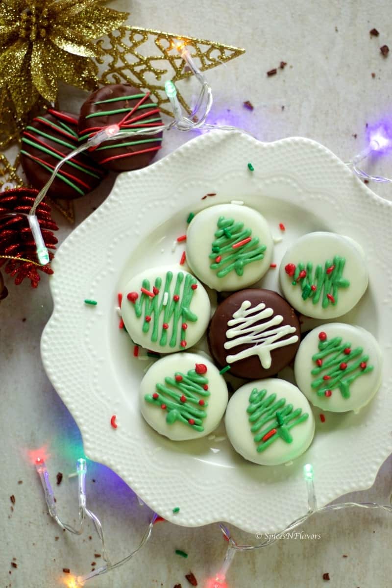 oreo cookies dipped in white chocolate arranged in a plate and surrounded by christmas decorations and lights