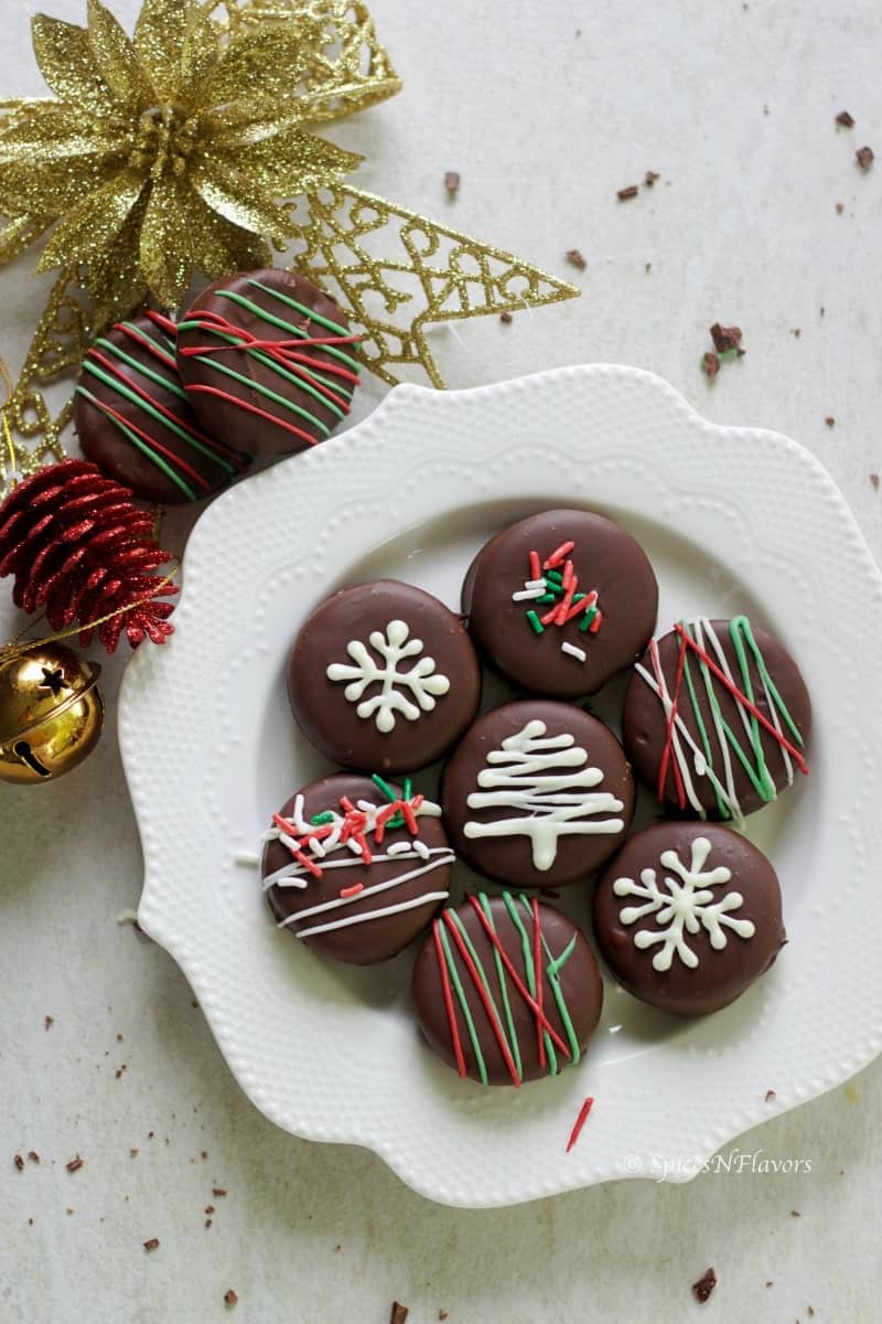 oreo cookies dipped in dark chocolate arranged in a plate and surrounded by christmas decorations