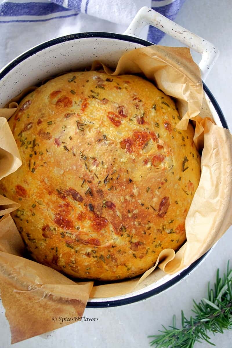 Instant pot no knead bread placed in a dutch oven with rosemary and a tea towel on the sides 