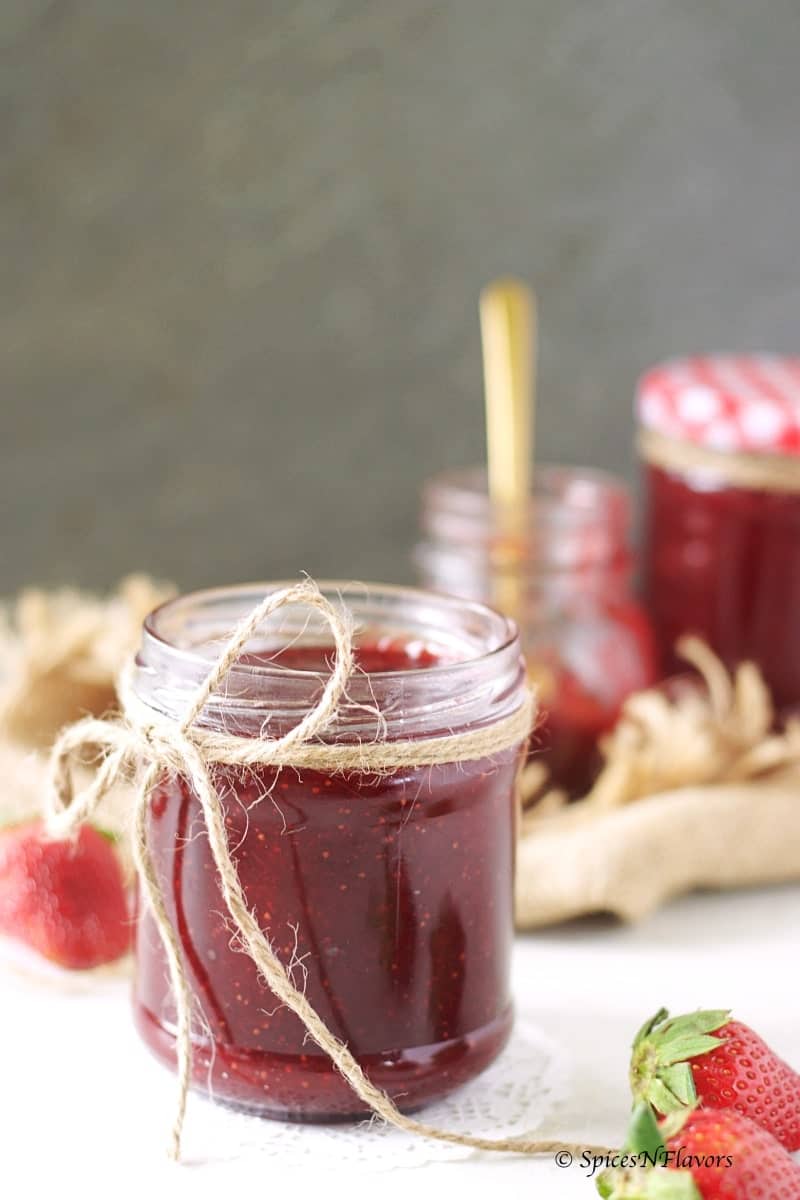 small mason jar filled with strawberry jam made in the instant pot in the front with another two mason jars kept behind in the backdrop