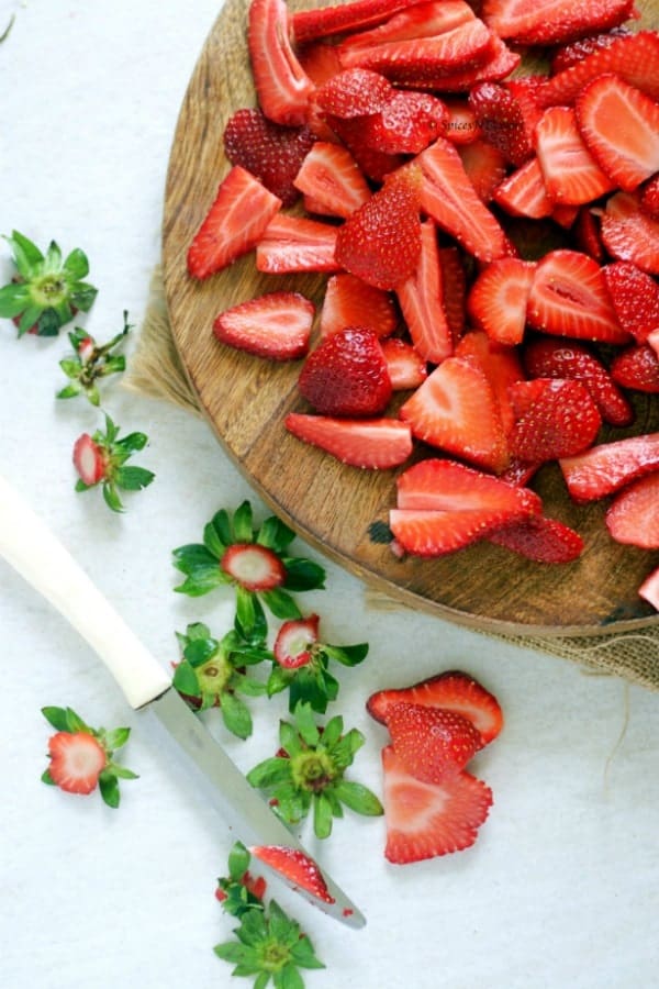 chopped strawberries placed in the wooden board with a butter knife and some scattered strawberry leaves 