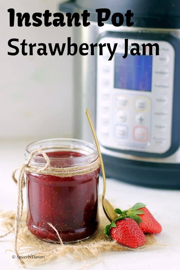 A small jam full of strawberry jam made in the instant pot with two fresh strawberries on the side and instant pot in the background