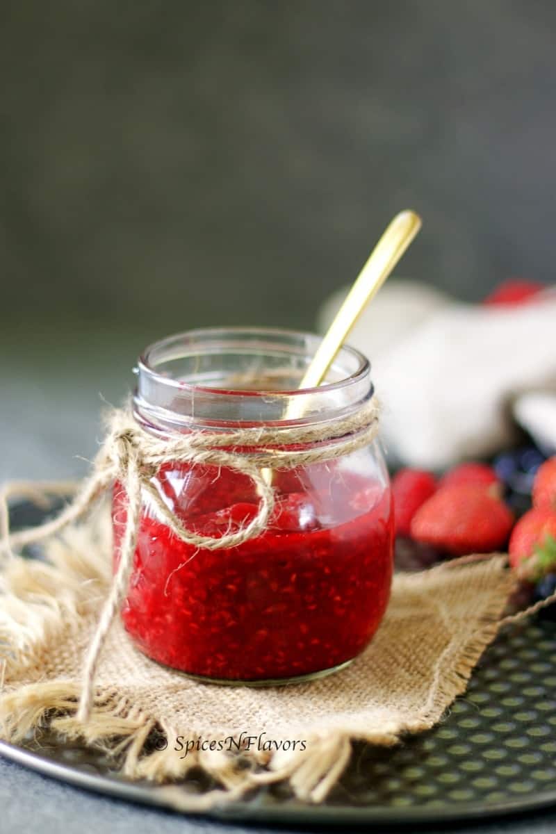 strawberry sauce placed in a mason jar with a spoon to be used as a topping for cheesecake