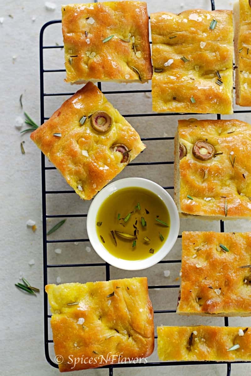 square pieces of focaccia bread placed on a cooling wire rack along with a bowl of herb infused oil