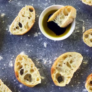 slices of ciabatta bread placed around a white bowl filled with olive oil