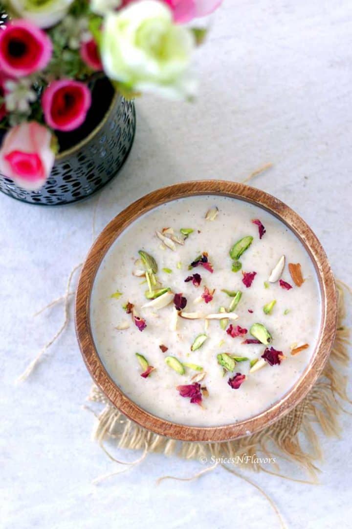 kheer served in a wooden bowl and garnished with pistachios, slivered almonds and rose petals