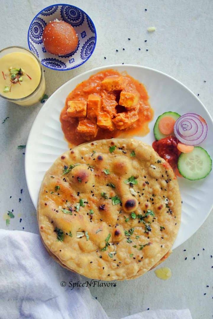 tandoori roti placed on a white plate with paneer butter masala and salad on the sides