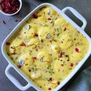 rasmalai pieces placed in a white square dish garnished with dried roses and nuts