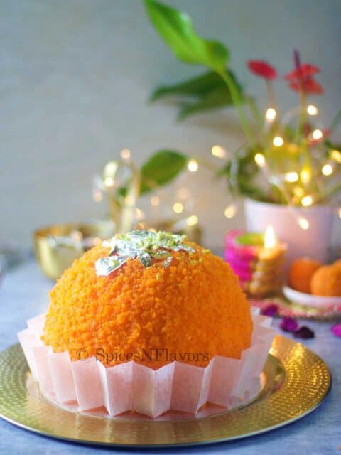 ladoo shape cake placed on a golden plate with lights and plant in the background