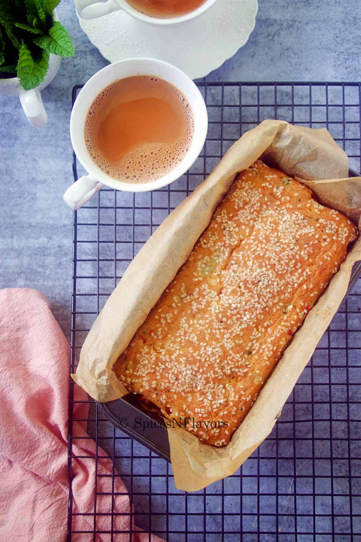 freshly baked cake sitting in the baking pan over a wire rack to cool accompanied by a cup of tea