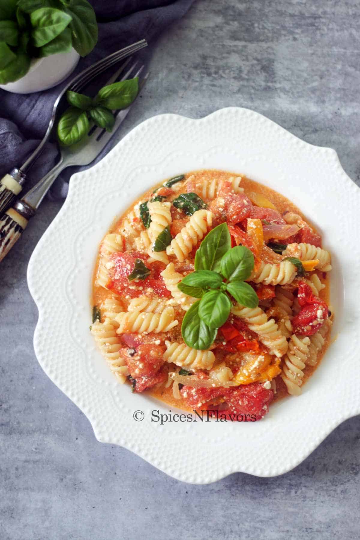 pasta served in a white plate garnished with basil leaves