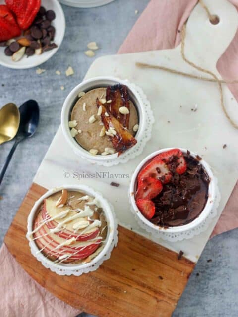 3 ramekins with different flavour of oats placed on a white marble chopping board