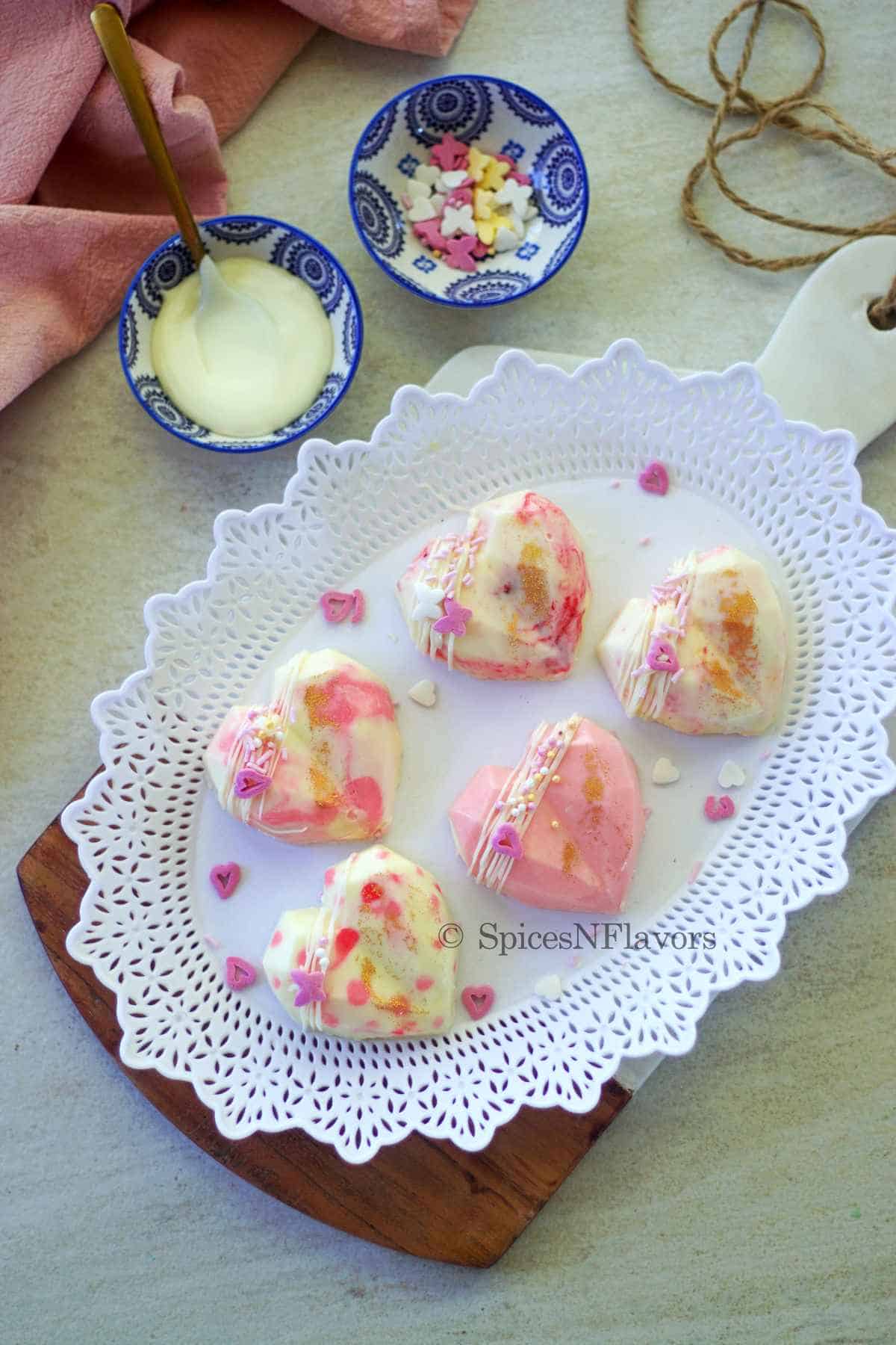 heart shaped cheesecakes placed on a white plate on top of a marble chopping board with melted chocolate and sprinkles on the side