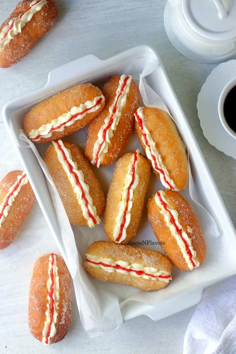 cream and jam filled doughnuts placed in a casserole with black coffee on the side