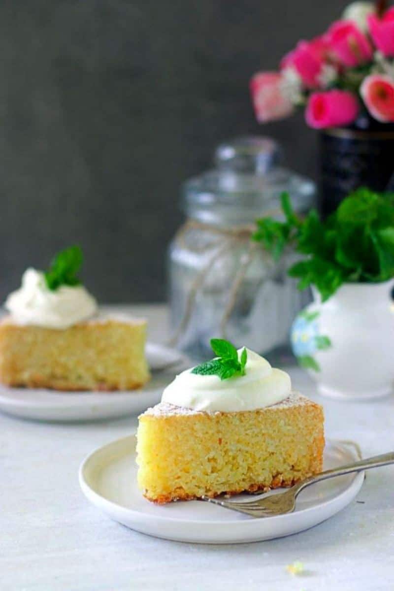 slice of rava cake placed on a white plate topped with softly whipped cream and mint leaves for garnish