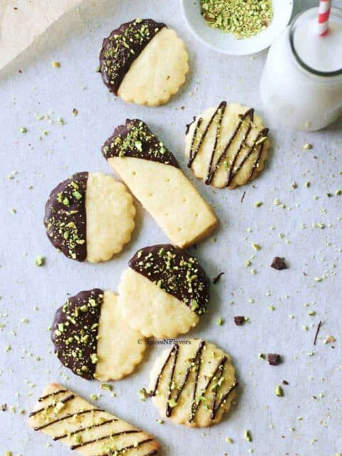 chocolate dipped cookies laid on a tile with milk and pistachios around it