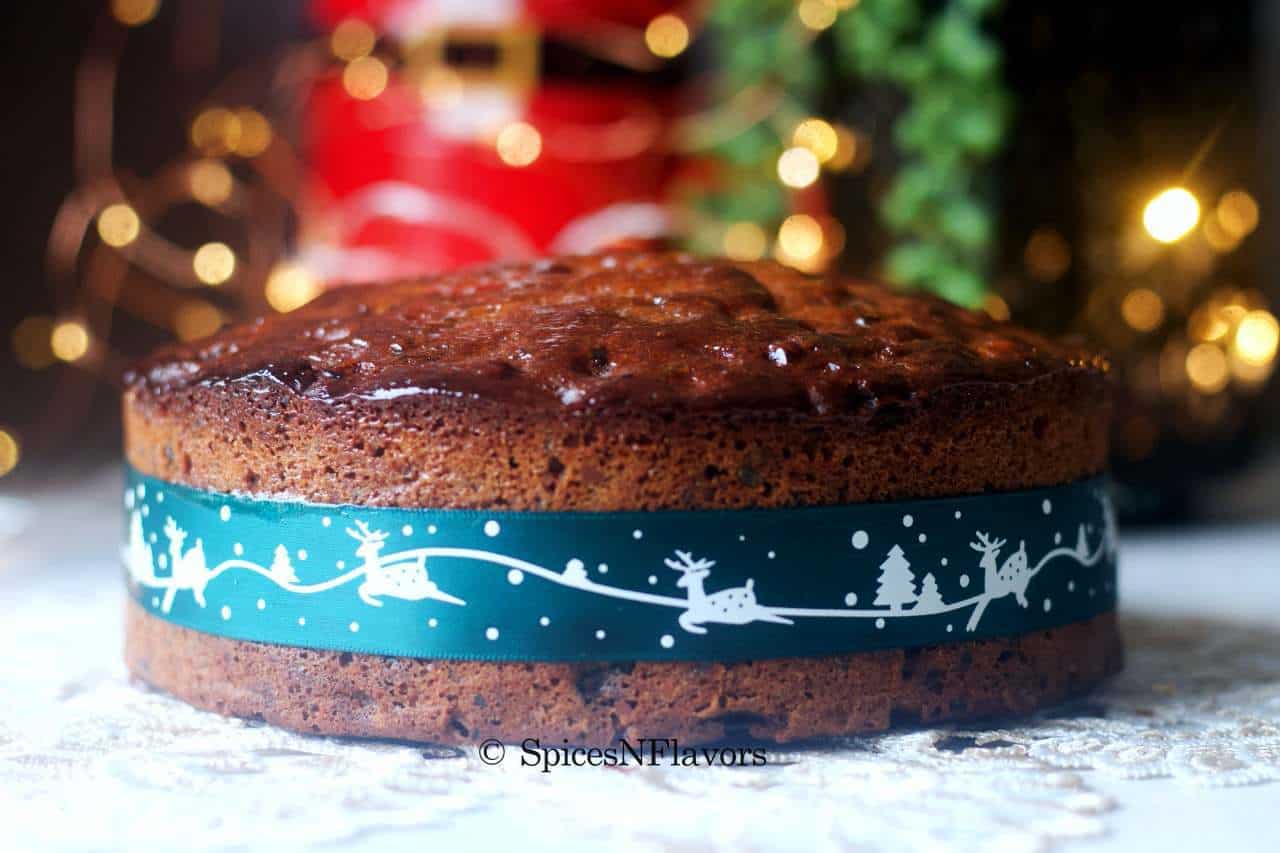 image of the whole fruit cake placed in the centre with lights, santa claus and tree in the background