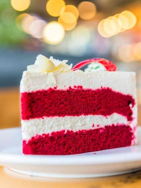 a slice of vibrantly coloured red velvet cake placed on a white plate with blurry background