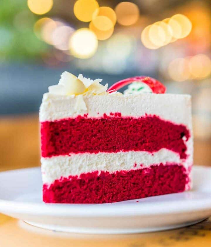 a slice of vibrantly coloured red velvet cake placed on a white plate with blurry background