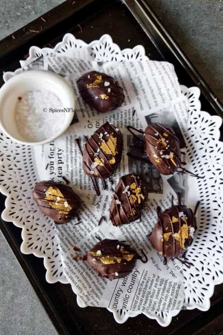chocolate covered dates placed on a white plate with sea salt in a bowl on the side