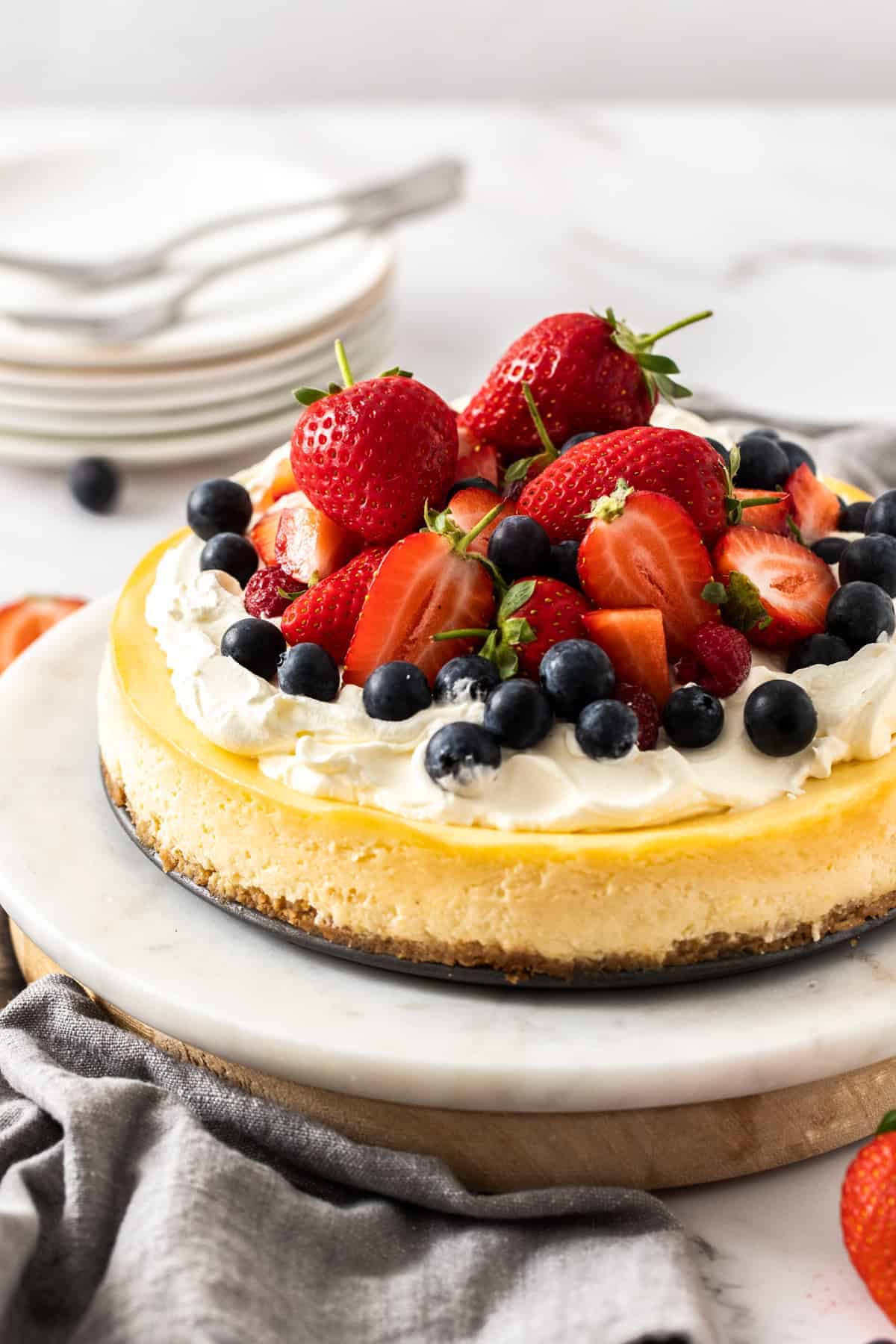 classic baked cheesecake placed on a cake stand with fruits on top