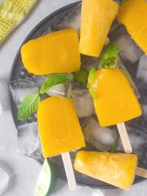 mango popsicles placed on ice bed with mint leaves for garnishing