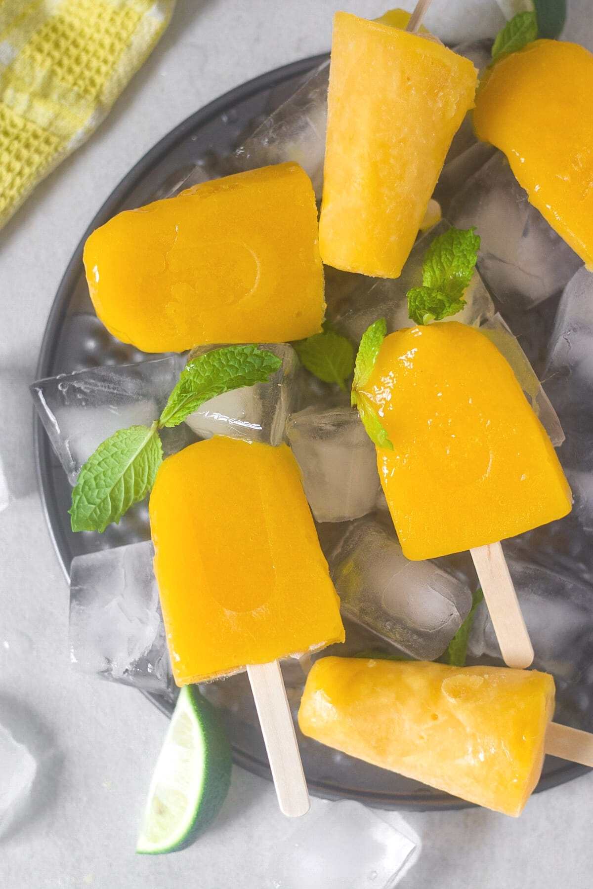mango popsicles placed on ice bed with mint leaves for garnishing
