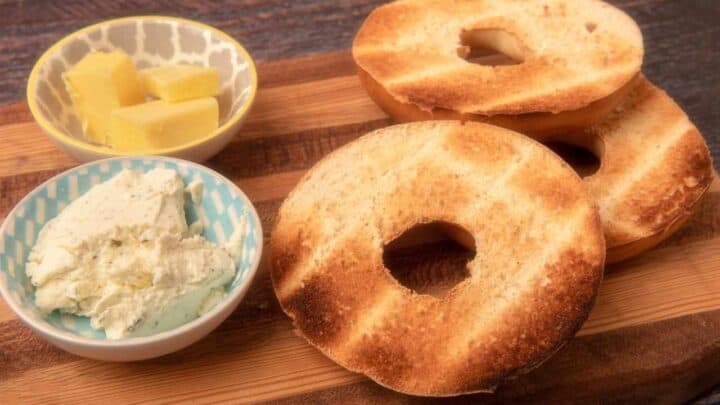 toasted bagels placed on a wooden board with 2 types of spread on the side