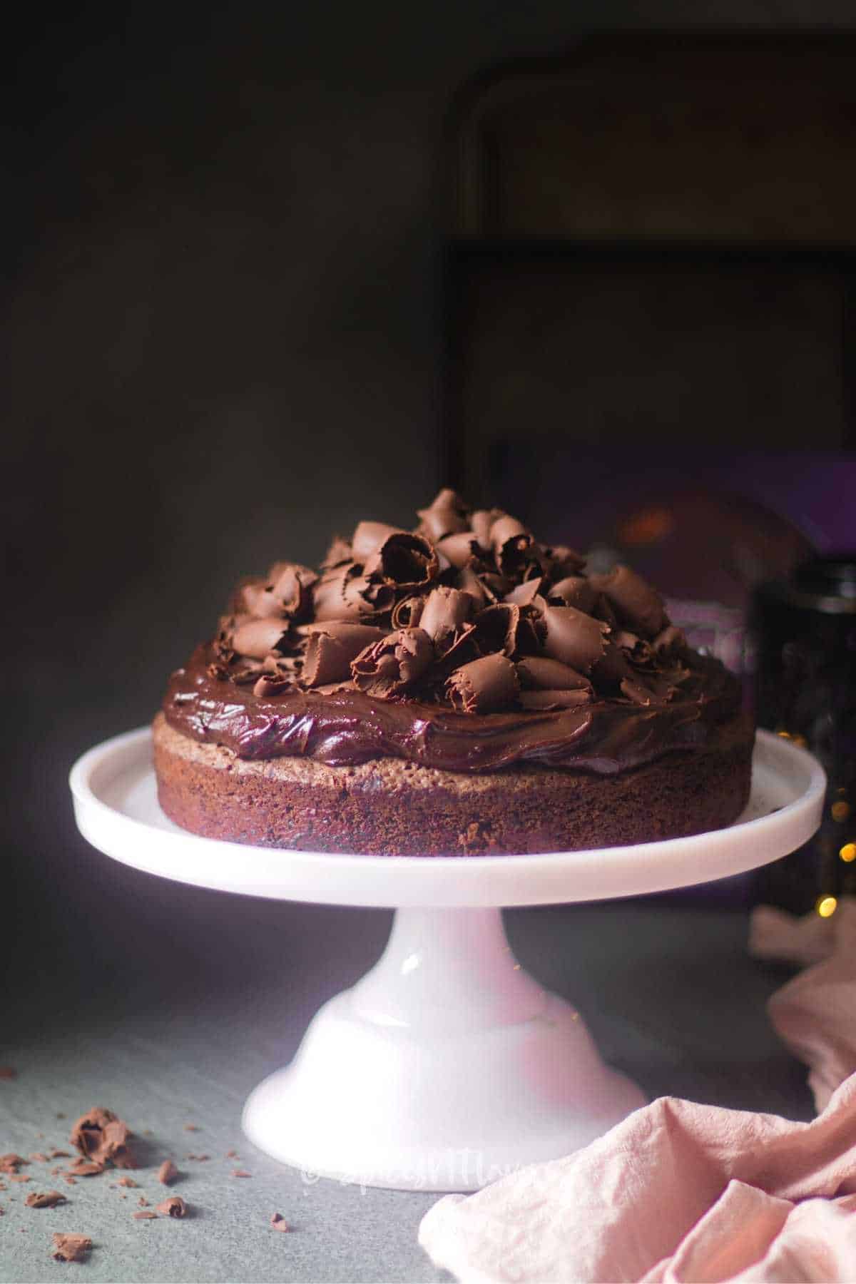 chocolate cake decorate with ganache and chocolate curls placed on pink cake stand
