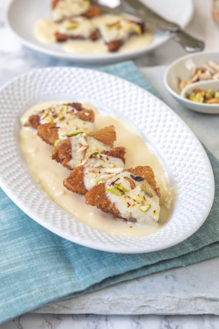 fried bread slices with rabdi placed on a white oval plate