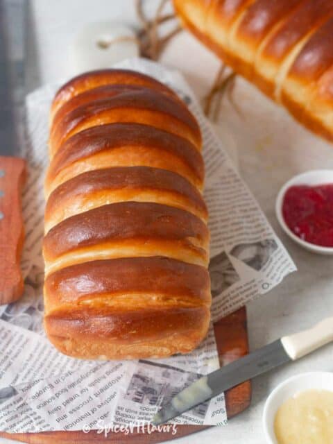 condensed milk bread placed on a newspaper printed parchment paper with jam and more condensed milk on the side