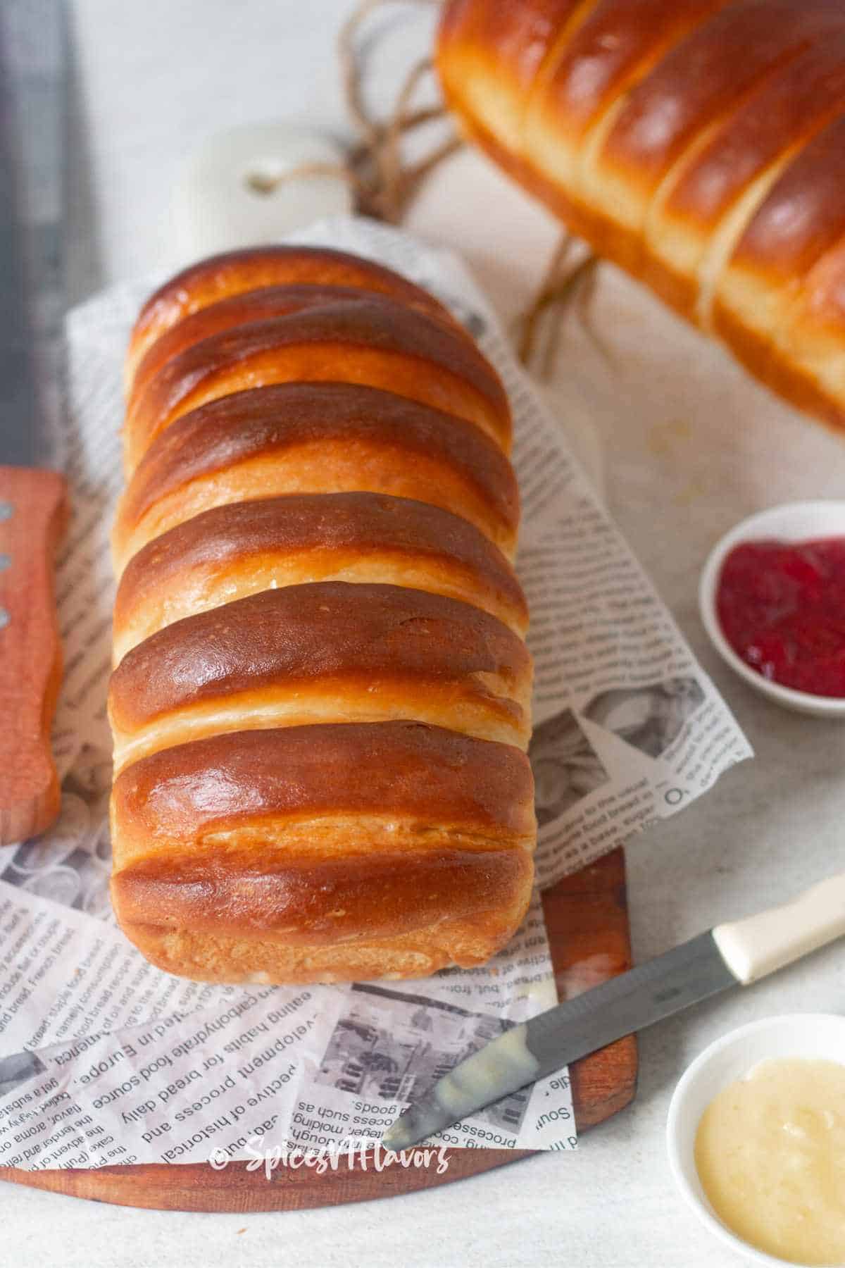 condensed milk bread placed on a newspaper printed parchment paper with jam and more condensed milk on the side