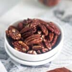 close up image of roasted pecans placed in white bowl to fit the recipe card