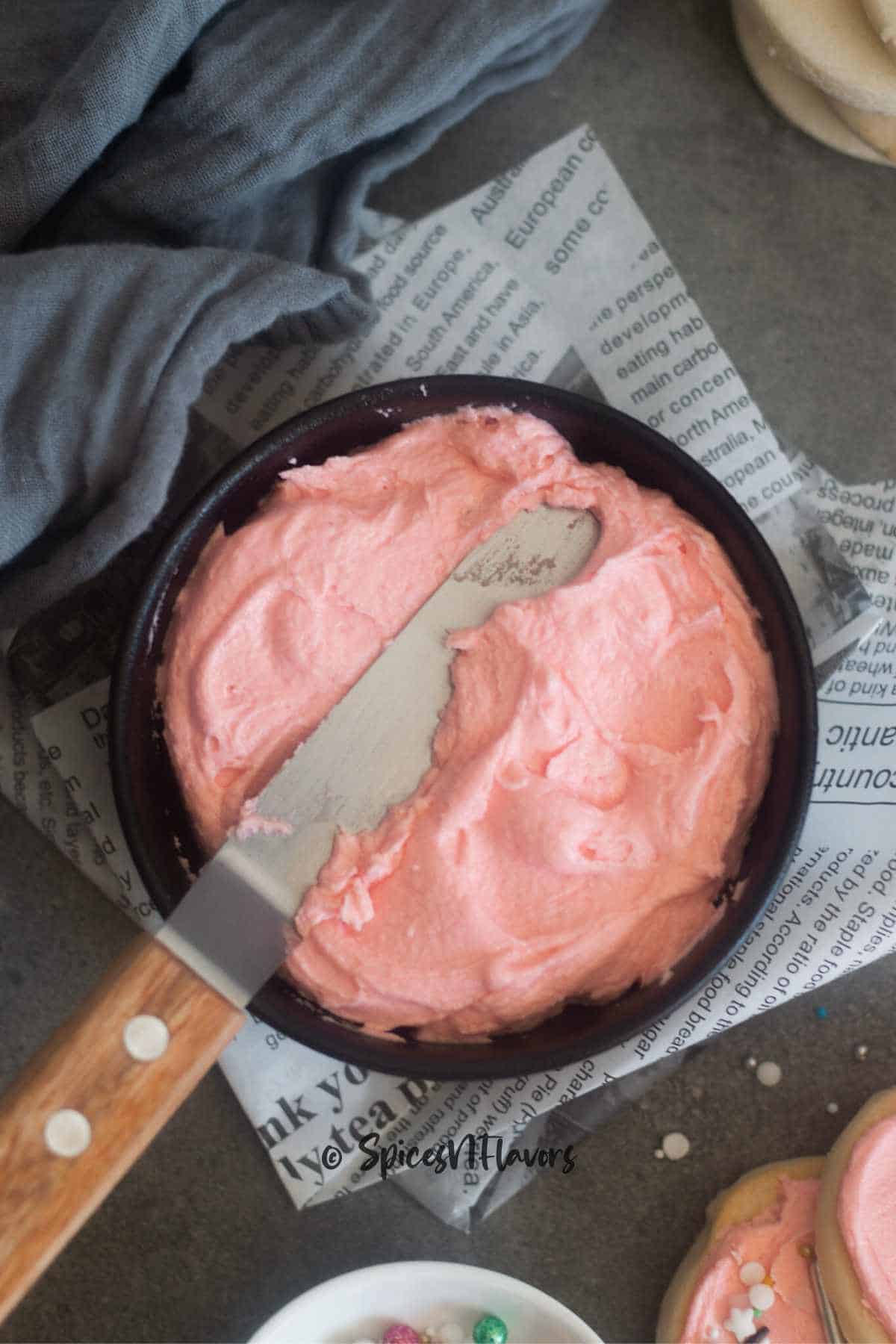 buttercream frosting placed on a black bowl alongwith an offset spatula