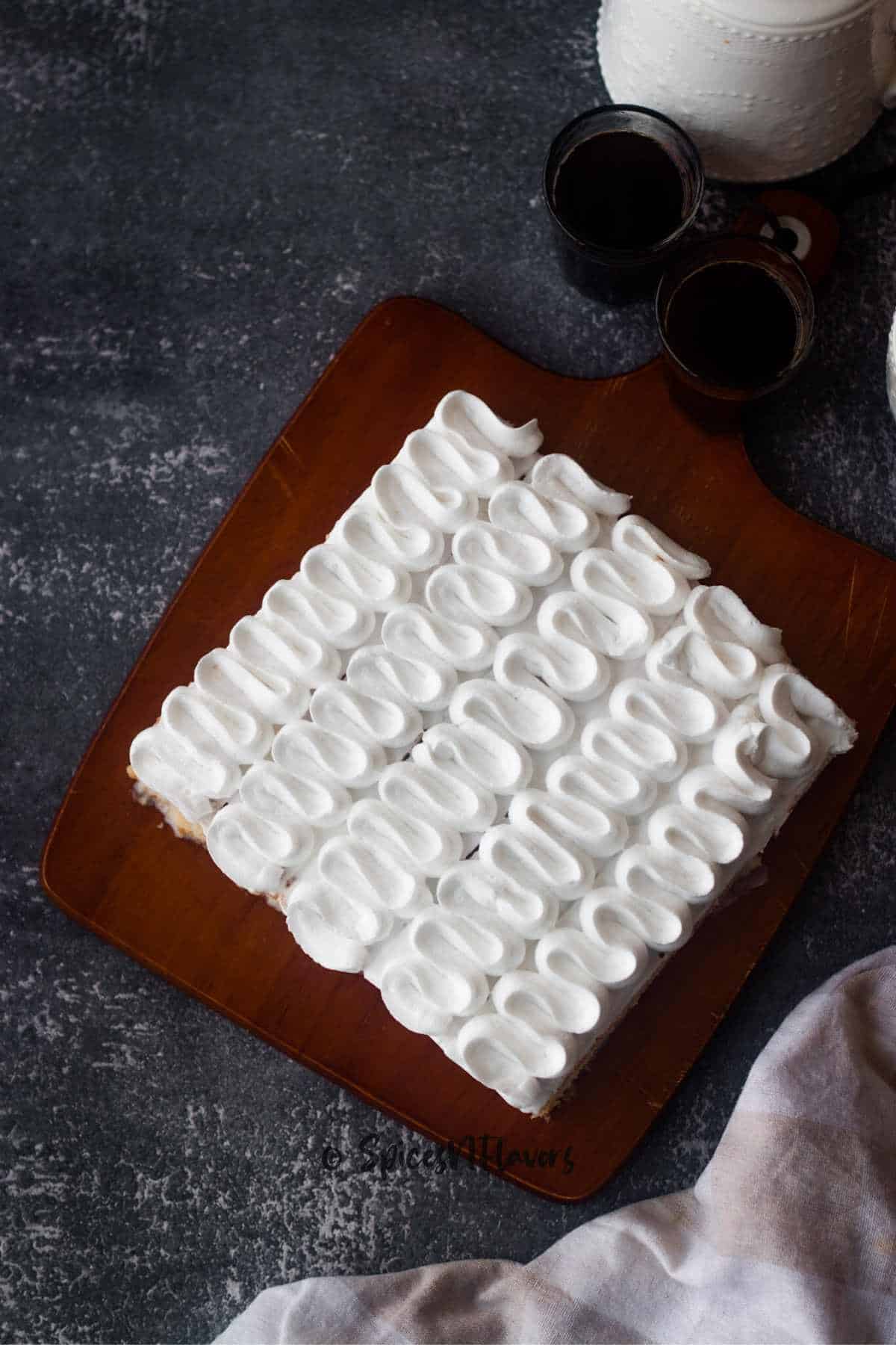 eggless tres leches cake frosted with whipped cream frosting and placed on wooden board