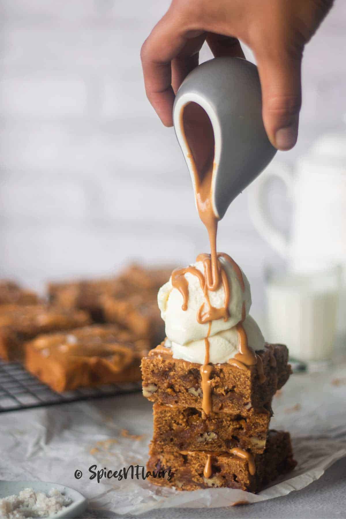 pouring butterscotch sauce over ice cream placed on stacked brownies 