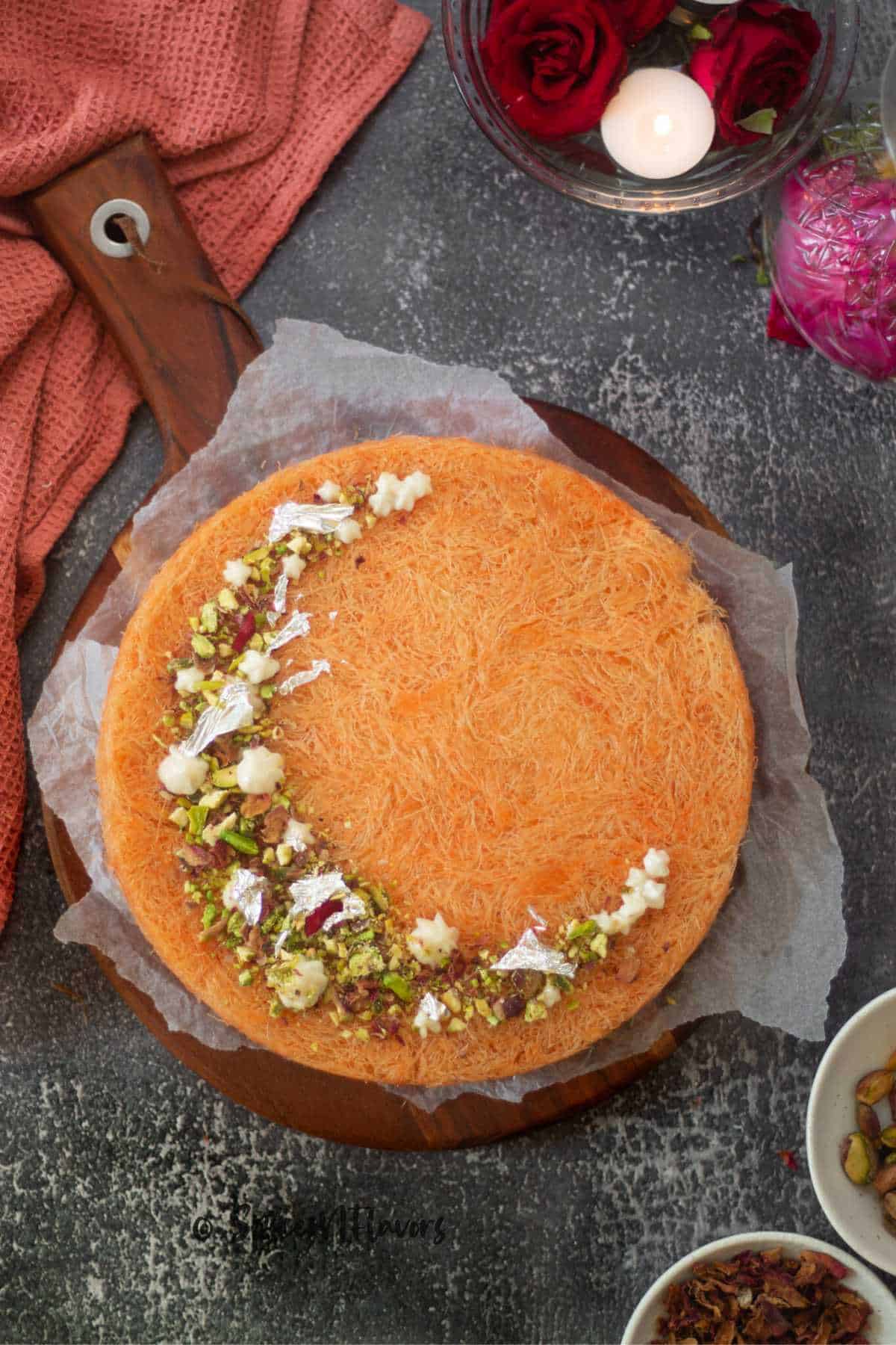 baked kunafa garnished with pistachio and rose petals placed on a wooden serving platter 