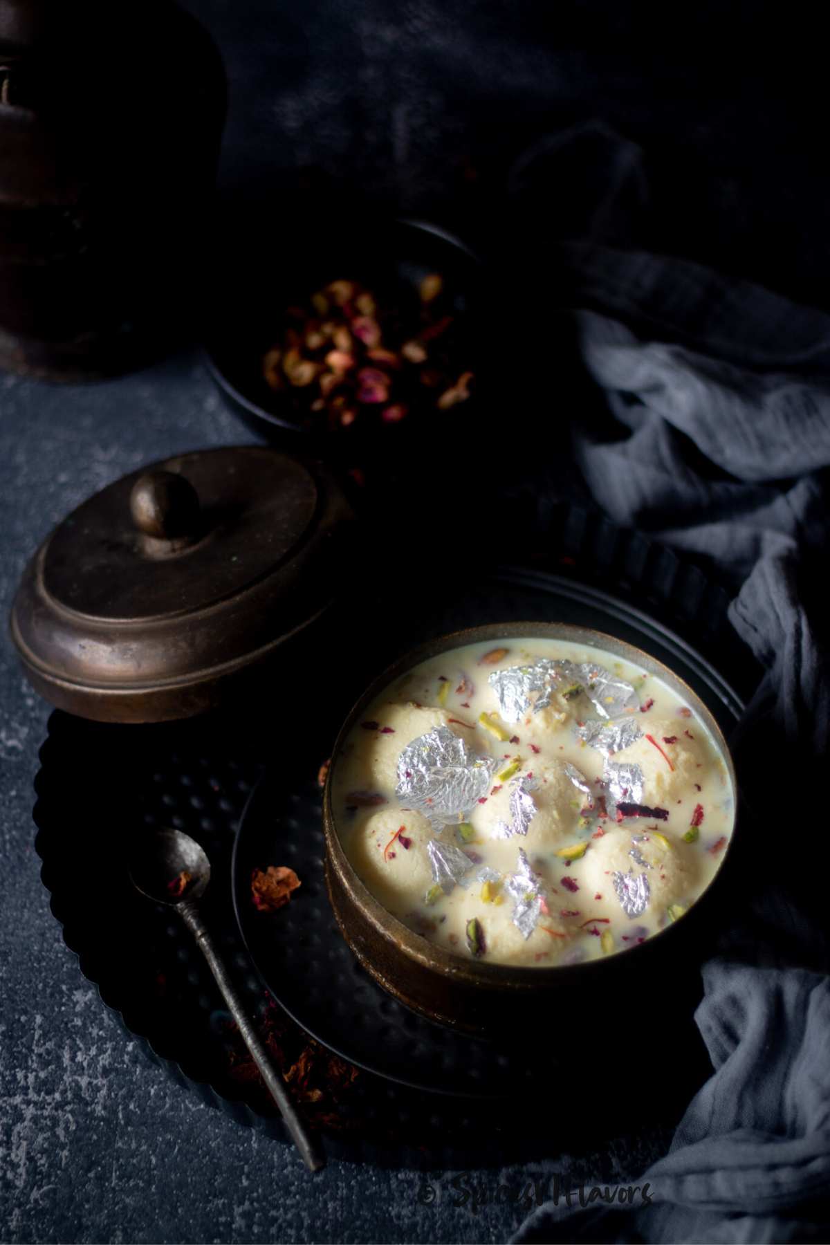 rasmalai using canned rasgullas placed in a box with pistachios placed in a black bowl in the background. 
