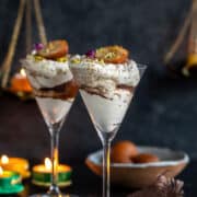 two wine glasses filled with cream and gulab jamun with lights and gulab jamun in the background