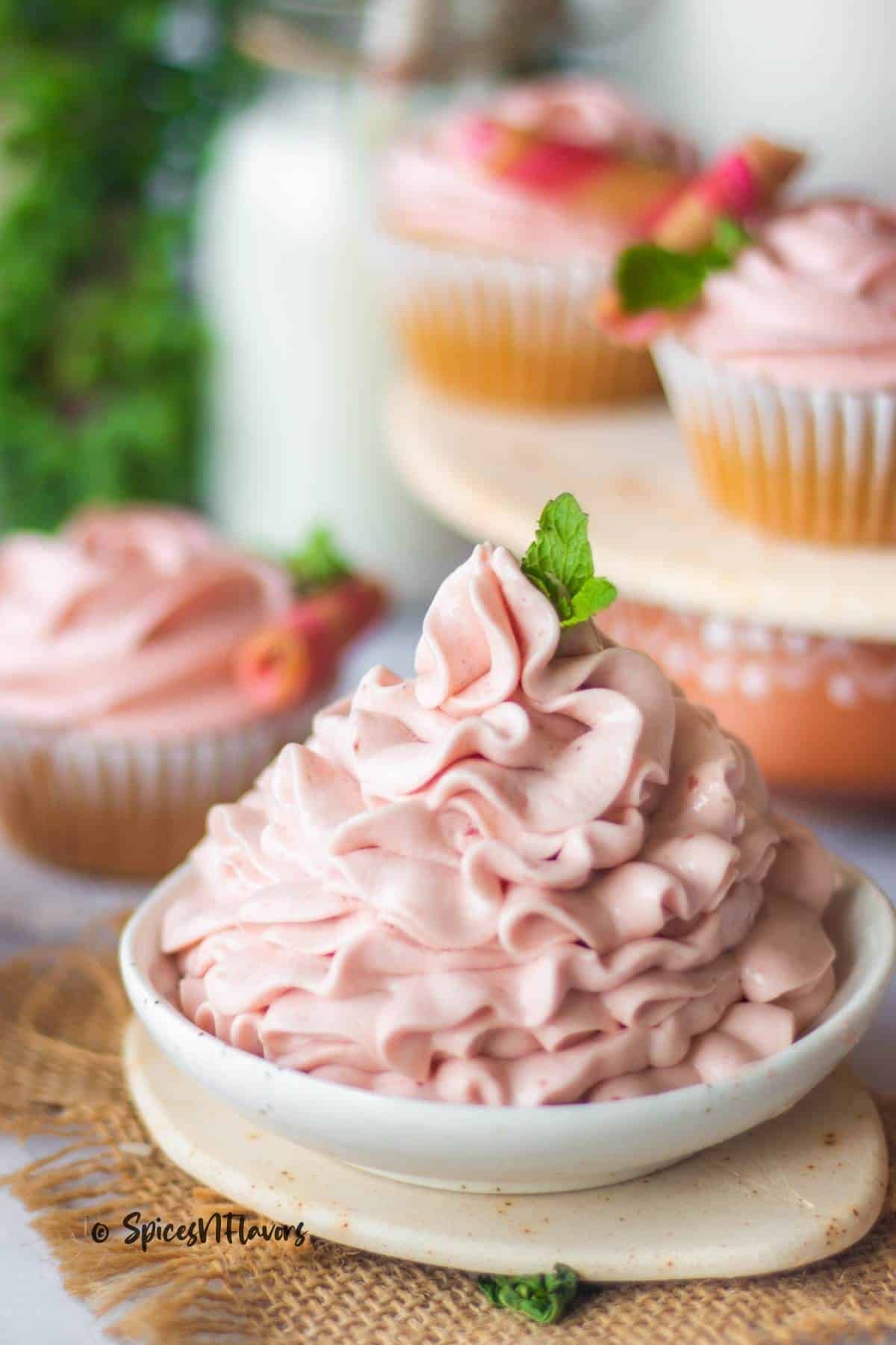 strawberry cream cheese filling piped on a white bowl with vanilla cupcakes placed in the background