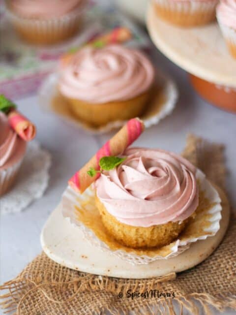 vanilla cupcakes frosted with strawberry frosting and a strawberry roll and mint leaf placed as garnish