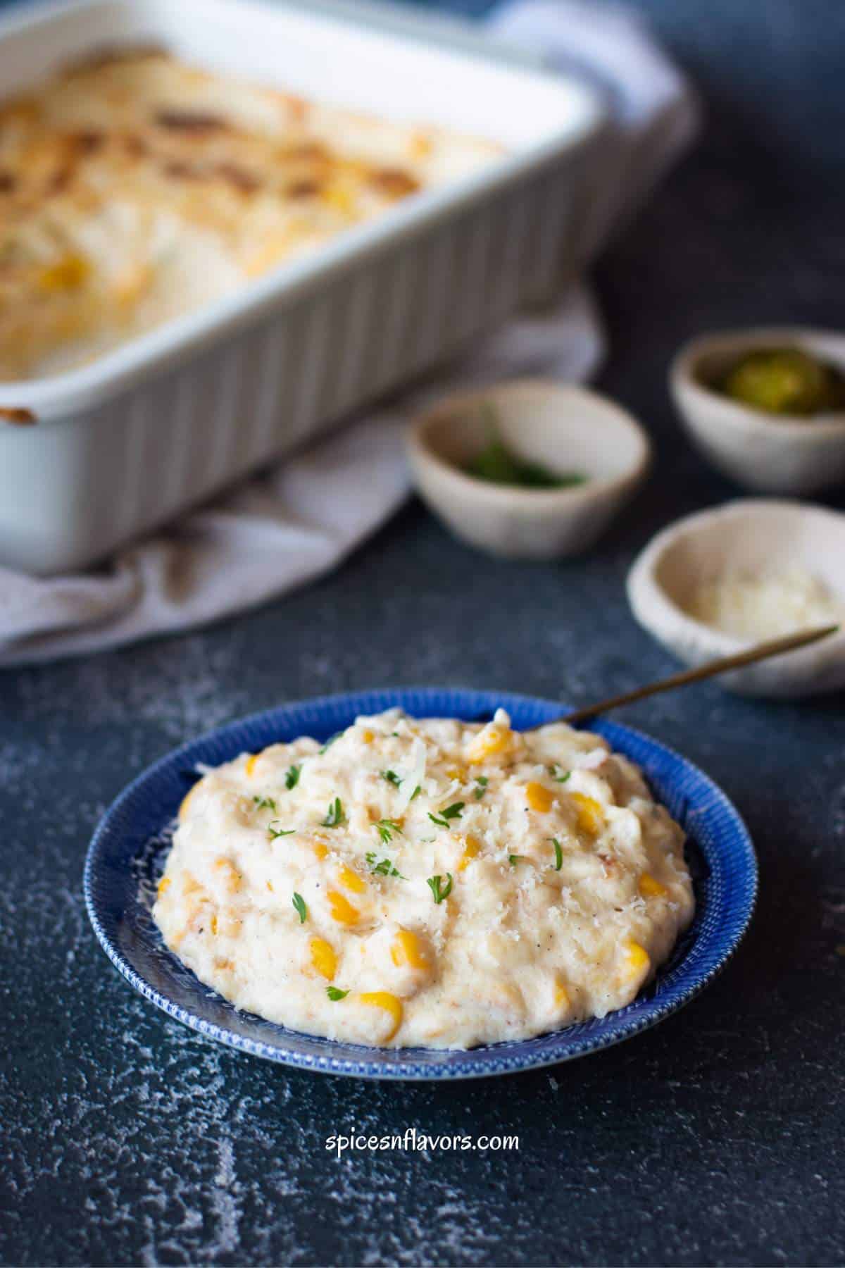 creamy corn casserole served on a blue plate with a garnish of cheese and herbs on top