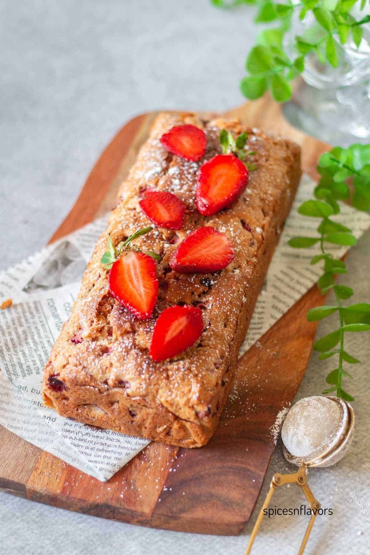 strawberry bread loaf placed on a wooden board with fresh strawberries on top