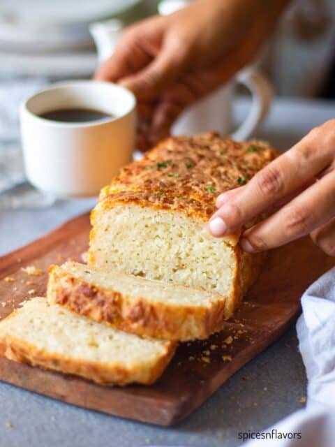 picking cheddar cheese bread with coffee on one hand