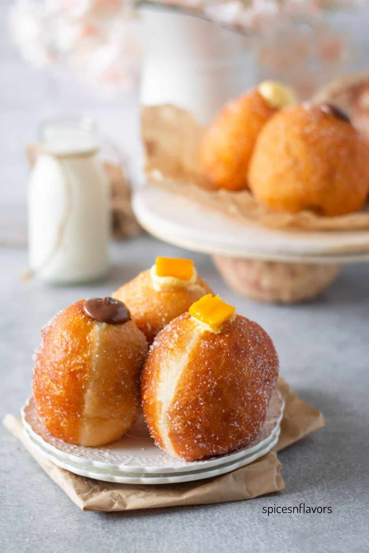 three eggless bombolonis placed on a white plate filled with cream and nutella